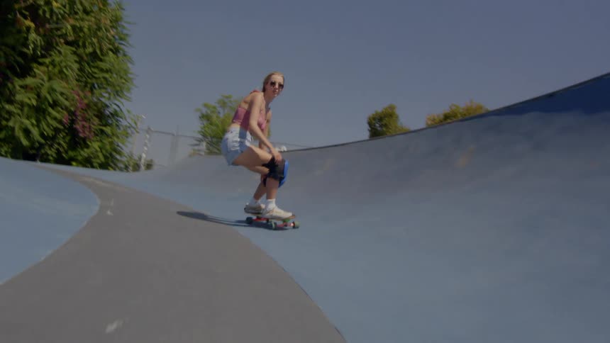 A blonde woman rides a skateboard while a man takes a video of her with his phone