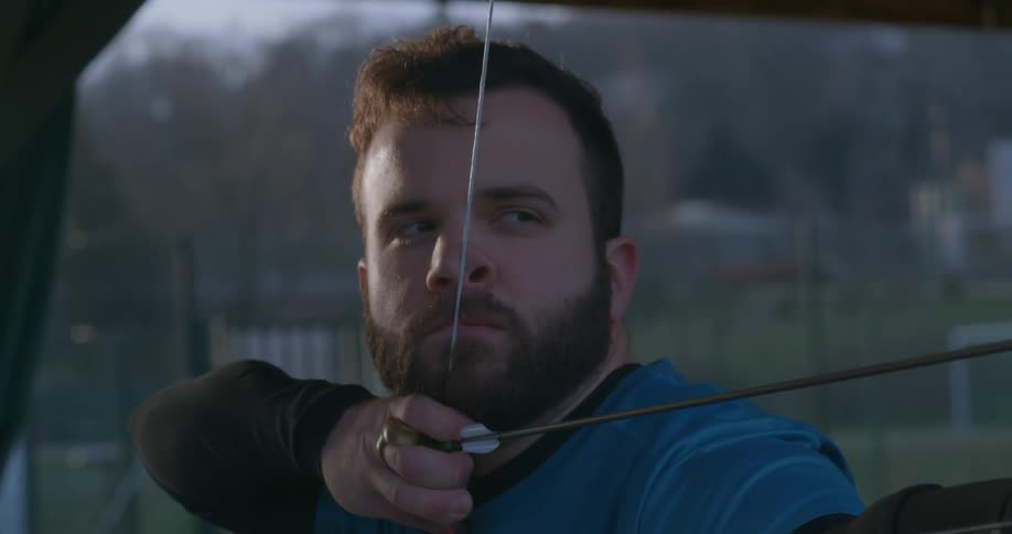 A man with a beard pulling the bowstring to his nose