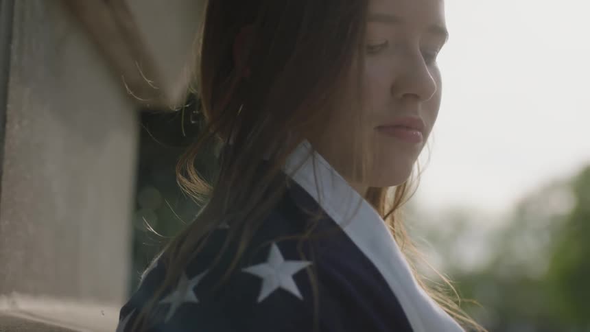 A woman is looking down wearing an american flag around her shoulders
