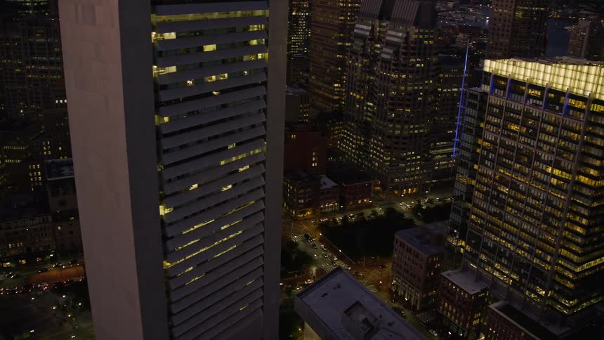 A huge building with the lights on and below is a busy street with several vehicles