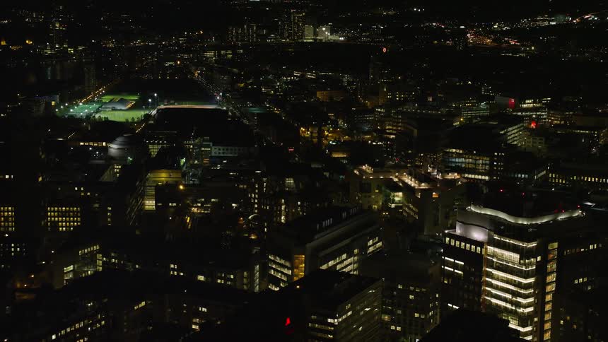 Aerial drone view of a sports arena and buildings in the downtown area of a city at night