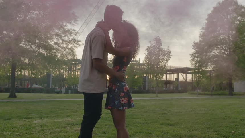 A man and woman hold each other with colored smoke moving past them