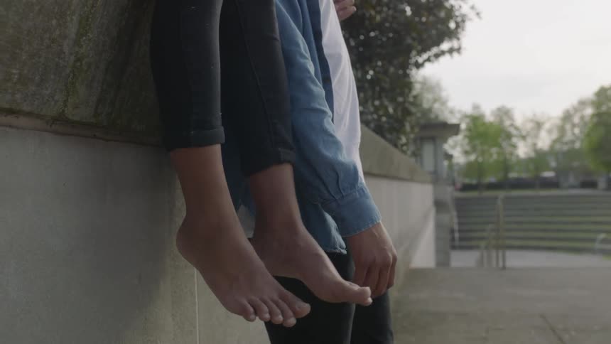 A man is leaning against a wall as another person sits on top