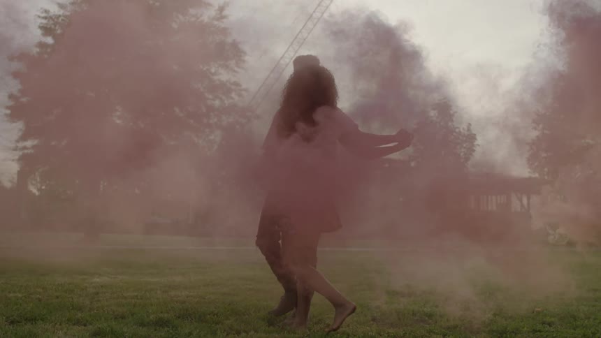 Two people dance with colored smoke around them