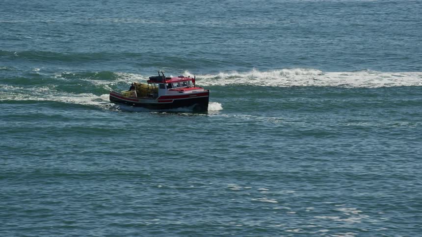 Small fishing boat sailing near the coast followed by waves