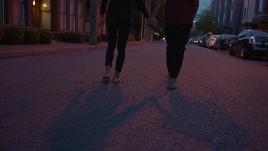 Two people walk down a street at dawn holding hands