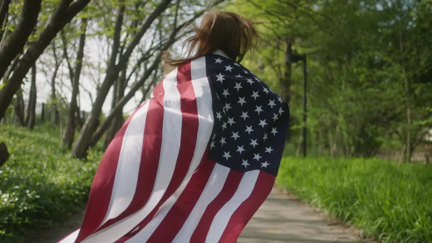 A woman is running outside with an american flag cape