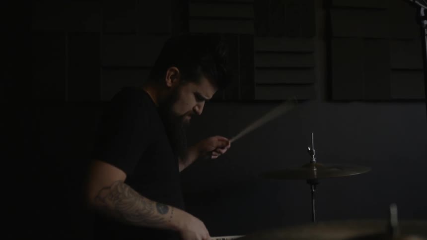 A man is playing drums in a dark studio