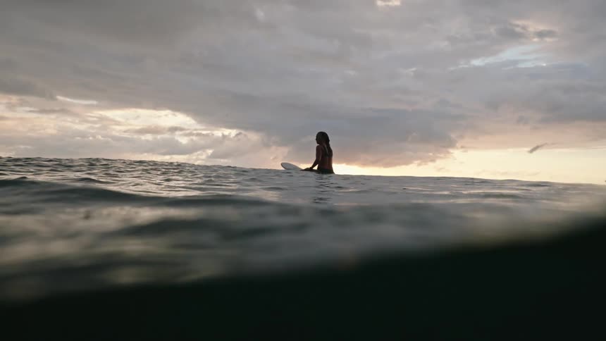 A female sits on the surf board on a sea