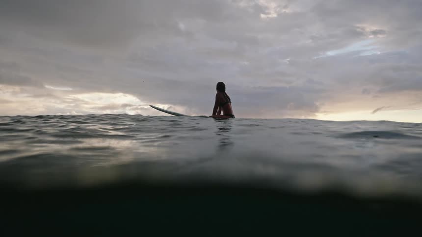 Lady sits on a board on the sea at sunset