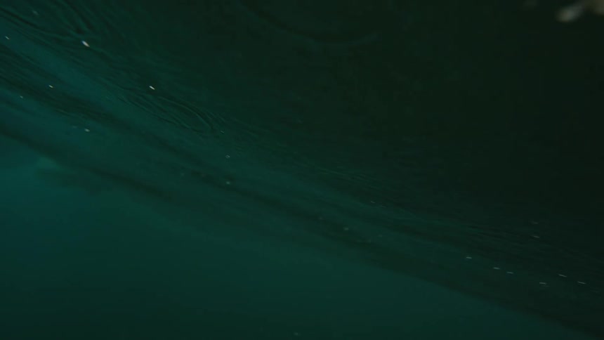A surfer stands on his surfboard as he rides a wave and the view changes to underwater