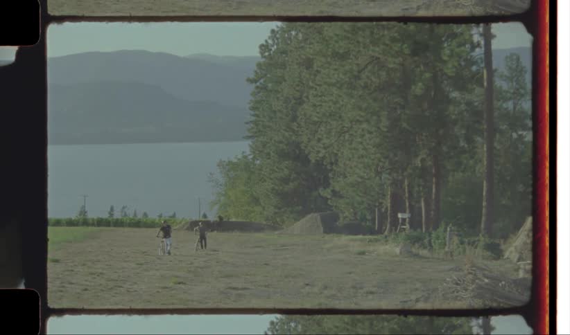 Three men walking while pushing their bicycles near a river at midday