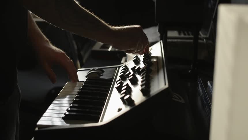 A man is turning knobs and playing a keyboard