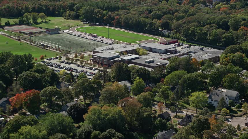 Aerial view of athletic field buildings trees and vehicles in parking lot