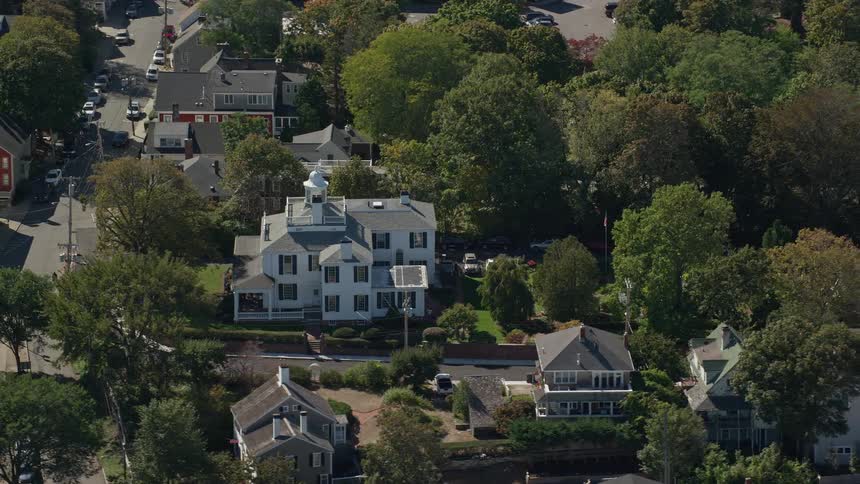An estate home on the corner of a neighborhood street is surrounded by trees and houses
