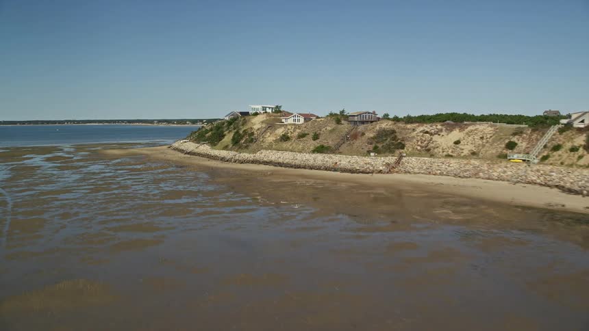 A beach with a house on top of the hills and the water is receding