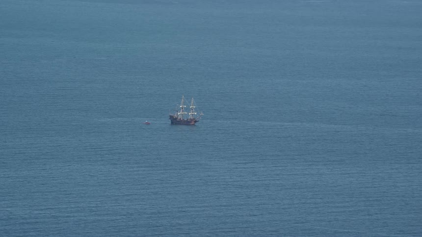 Tugboat pulls sailing ship through ocean on foggy day