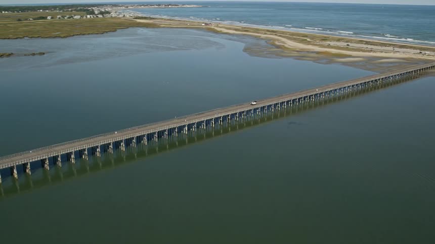 Red car crosses a bridge over a lake next to the ocean