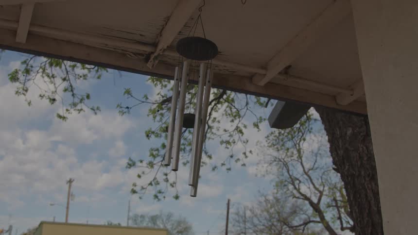 A wind chime swings from the woodwork of the house