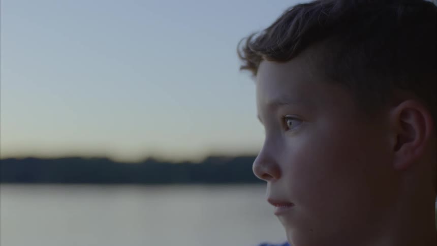 Close up of boy skipping rocks at dusk