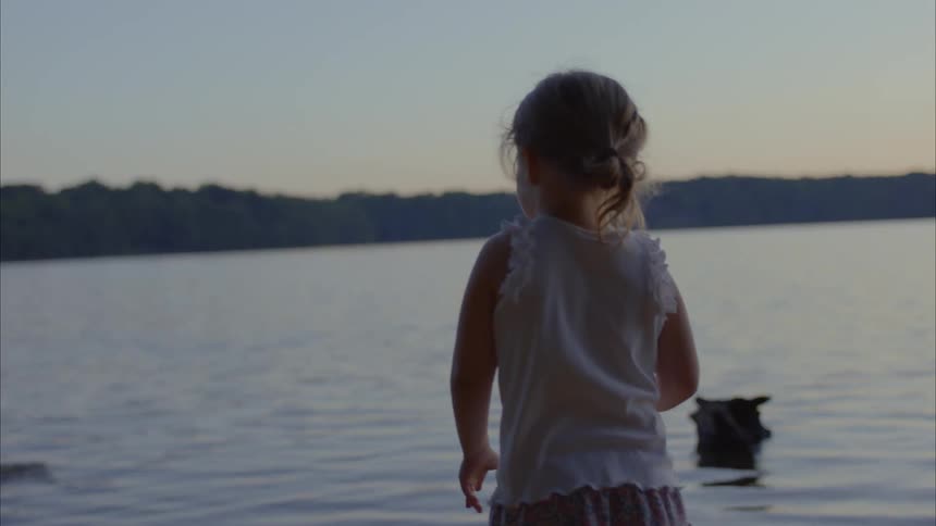 Little girl skipping stones in the river at dusk