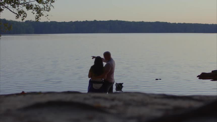 A man and a woman embracing and facing the sunset by a lake