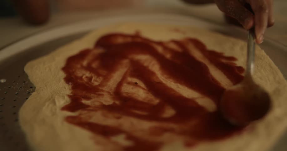 A hand holding a spoon and spreading tomato sauce on pasta