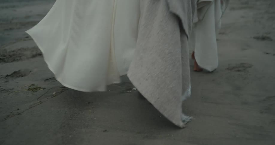 Three people covered in robes walking by the beach at sunset