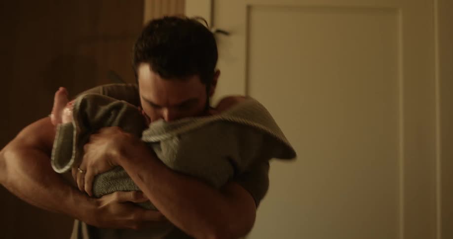A man with a beard playing and kissing his son wrapped in a towel