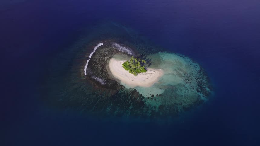 A small island of sand and little vegetation surrounded by a blue sea