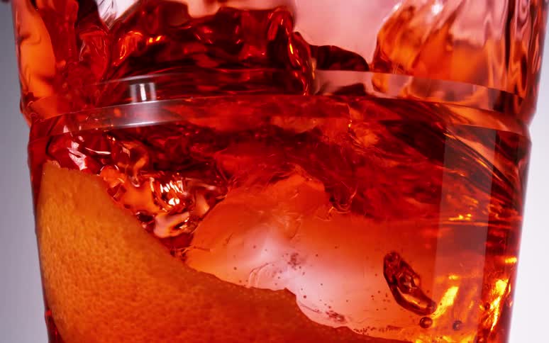 A square transparent piece of ice falling into a red liquid and making waves inside the glass