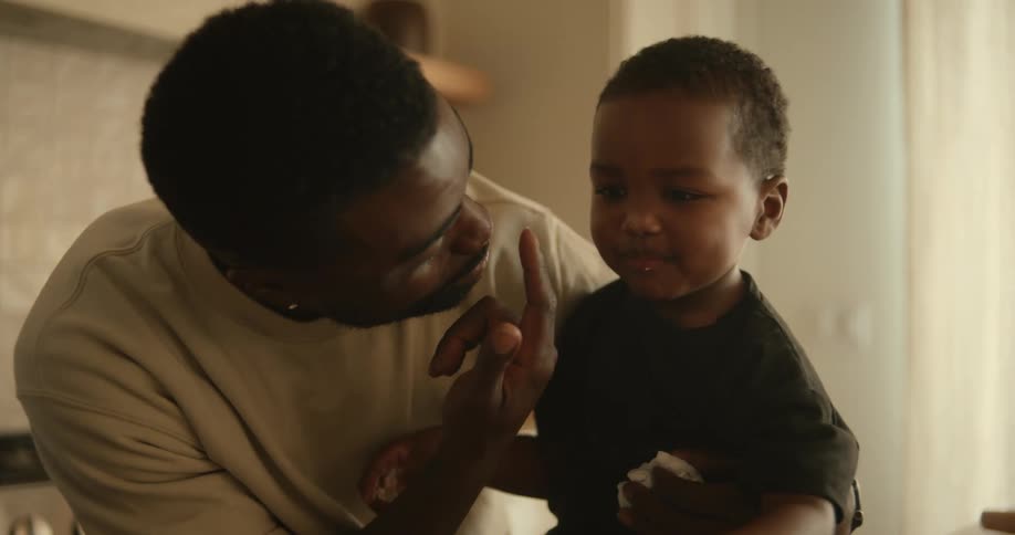 Father and son pointing fingers to each others noses while indoor at midday