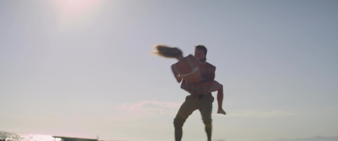 A man and a woman is having fun time in the beach as the man spins the woman around while carrying her in a sunny day