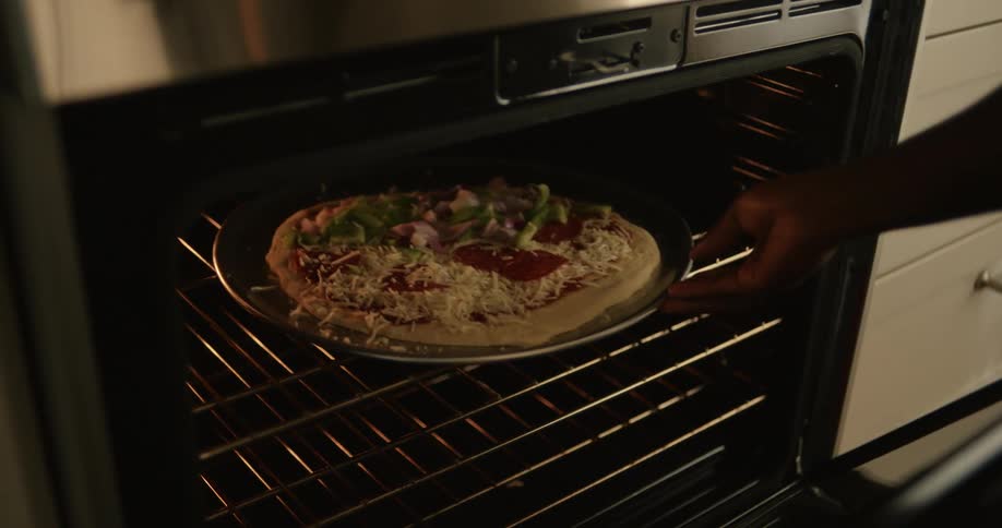 A man with a child on his lap puts a pizza in the oven and claps hands with the child in celebration