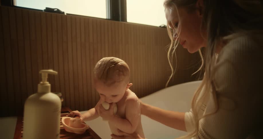 Mother bathes her baby in the tub at home