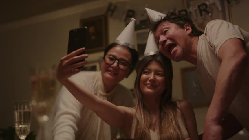 A young girl taking a photo with her parents wearing hats at a birthday party