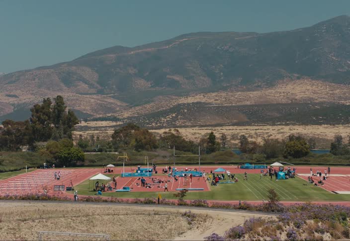 People are walking around a sports field by a mountain