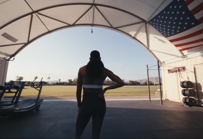 A woman stands in a gym overlooking a field