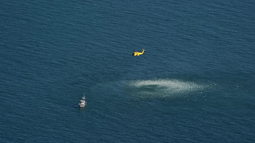An yellow helicopter hovering in the middle of the ocean next to a boat