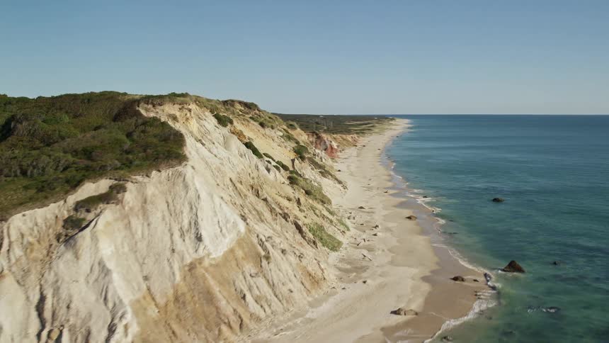 A canyon stands alongside a lake as waves roll over the beach with a coastal neighborhood