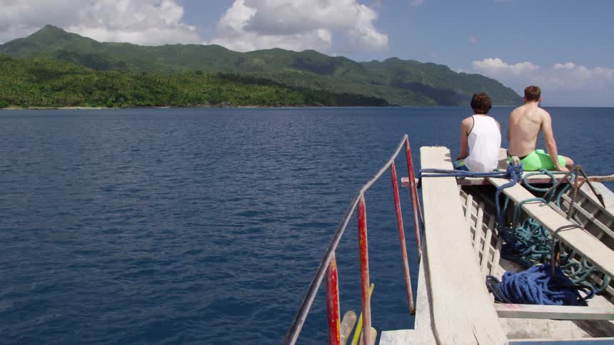 Two people sit on a boat as it sails ahead