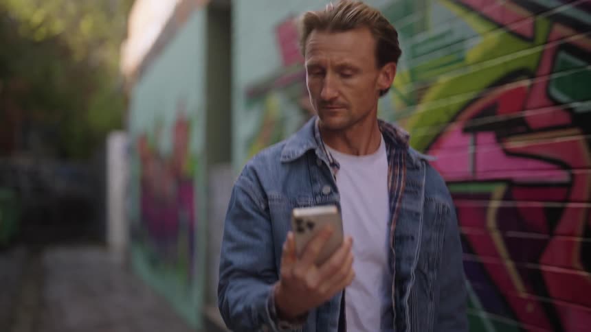 Man walks on an alley filled with graffiti holding a phone