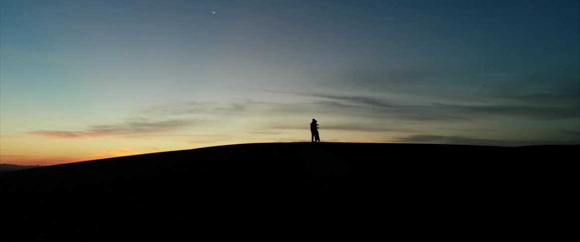 Silhouette of two people standing on a hilltop hugging and embracing each other