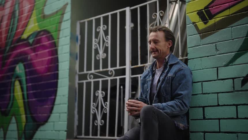 A man is sitting by the building drinking coffee