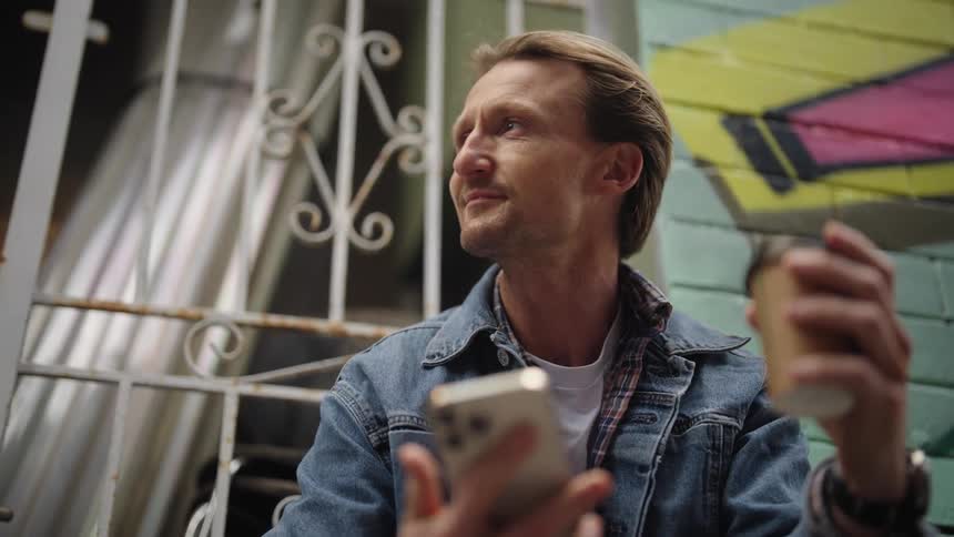 Man checks his phone while drinking coffee on the street