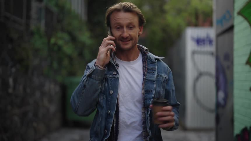 Man walking through alleys drinks coffee while talking on the phone