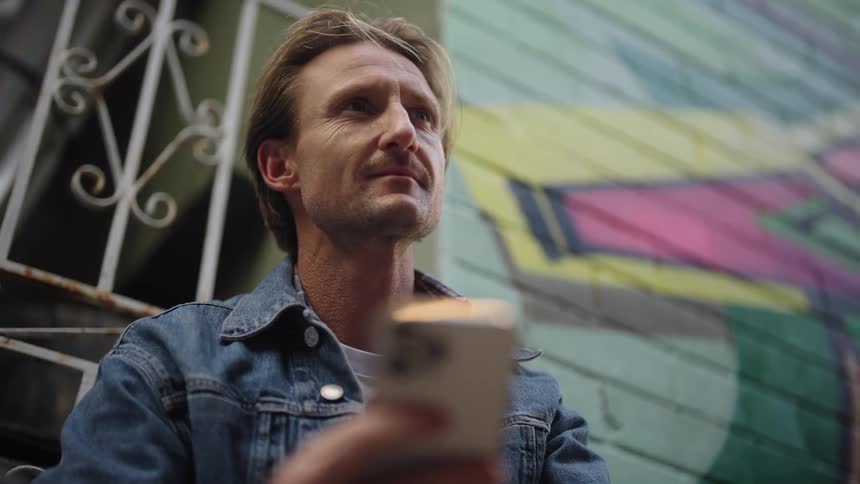 Man smiles while drinking coffee and texting on smartphone