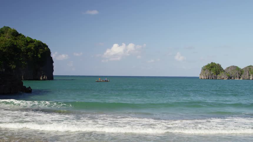 Waves crash against the shore with a boat in the distance