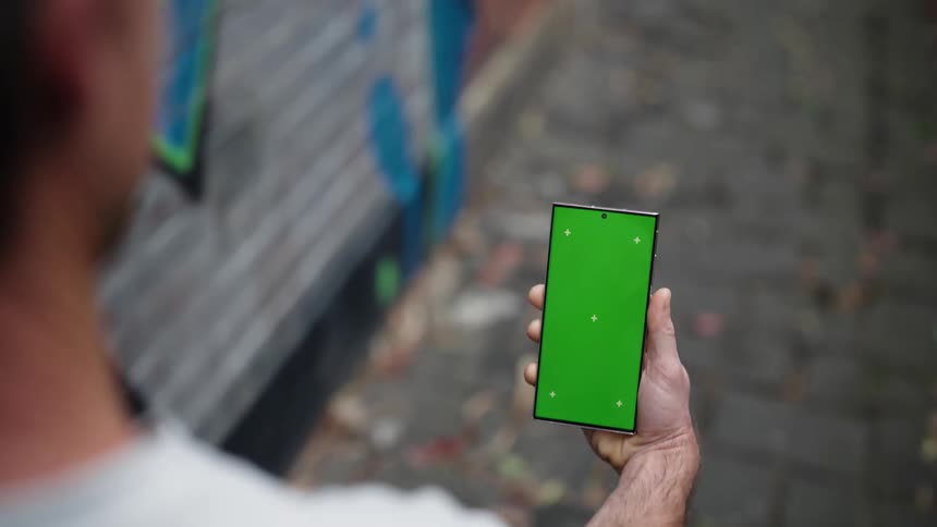 A person walks with a cell phone with a green screen in their hands
