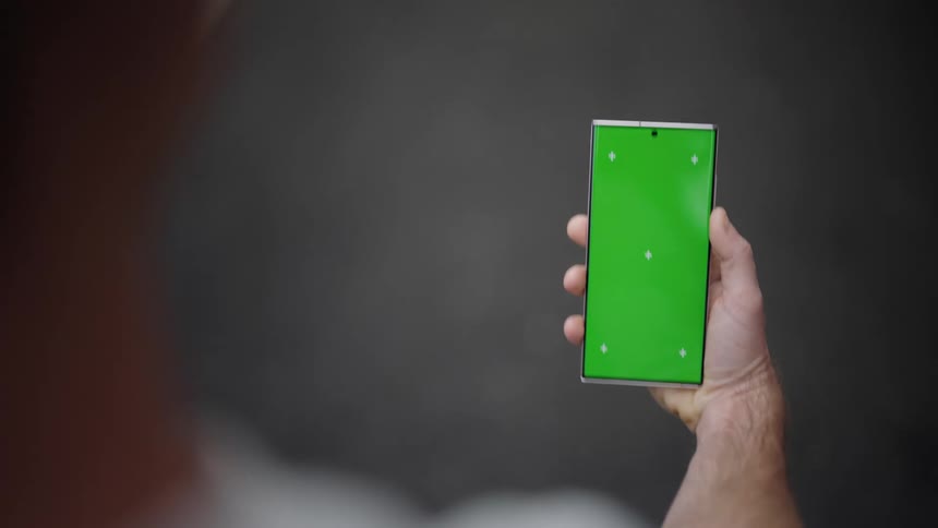A man walks while looking down at the mobile phone on his right hand